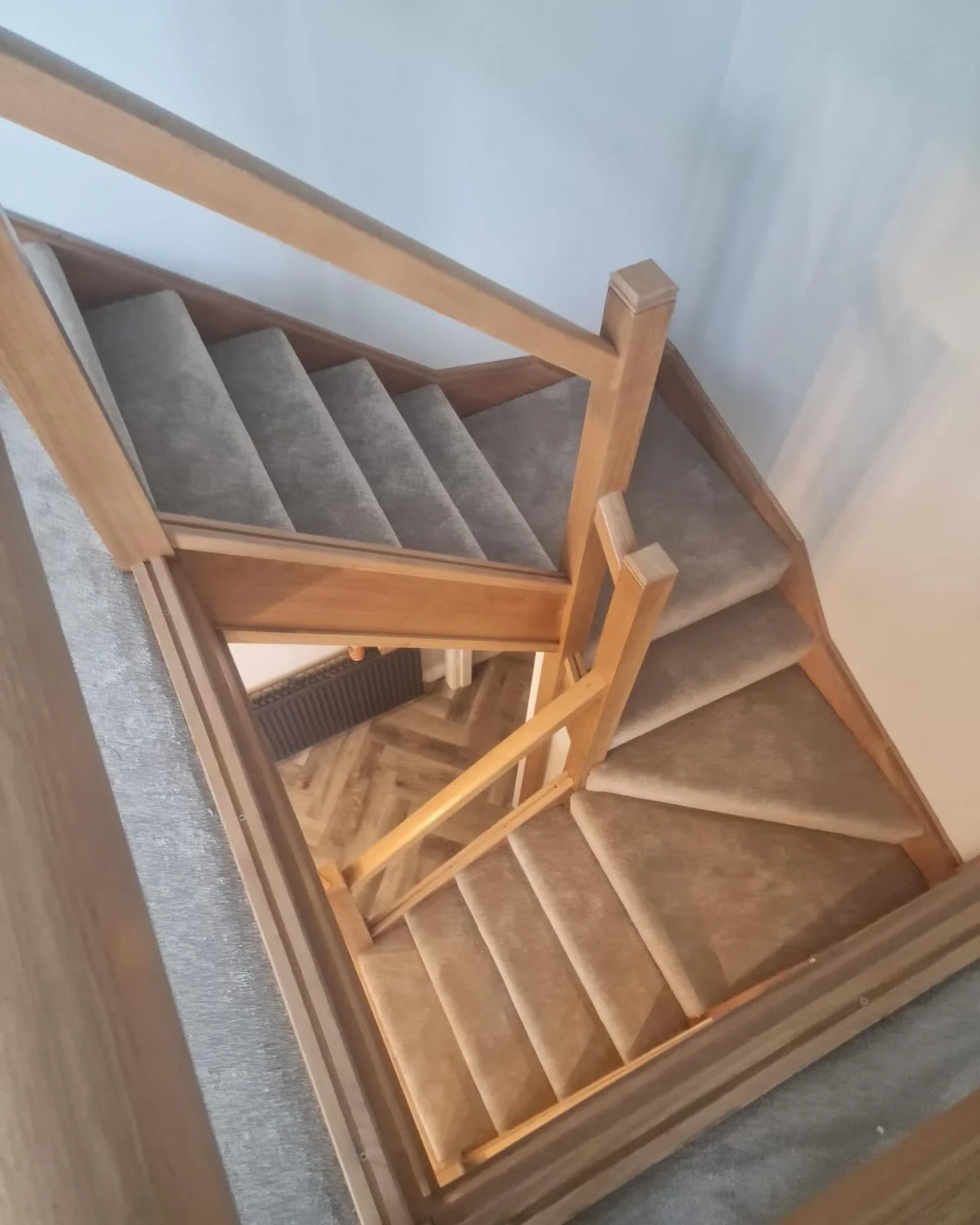 Grey carpet on a turning staircase with wooden handrails